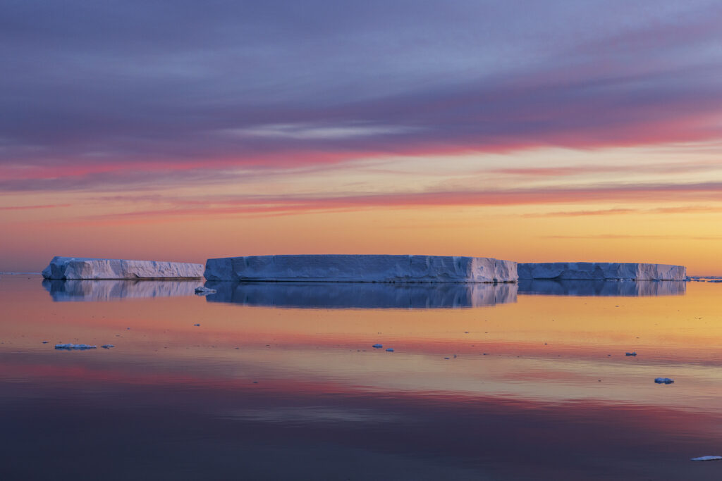 A Trio of Tabular Icebergs Reflected at Sunrise on the Solstice